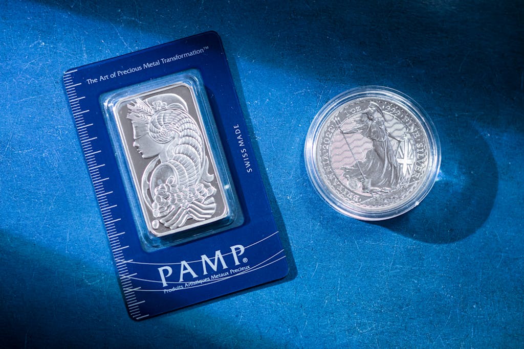 Close-up of a silver coin and a PAMP bar on a blue textured background emphasizing wealth.
