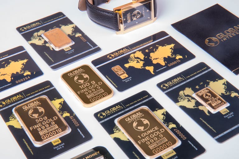 High-angle shot of fine gold bars with a luxury watch and branded packaging.