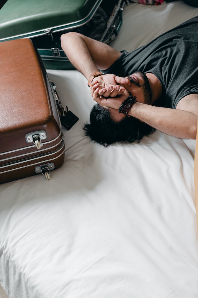 A young man rests on a bed, surrounded by luggage, reflecting a travel or moving theme.