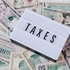 US dollar bills surrounding a sign showing 'TAXES'. Ideal for financial context.