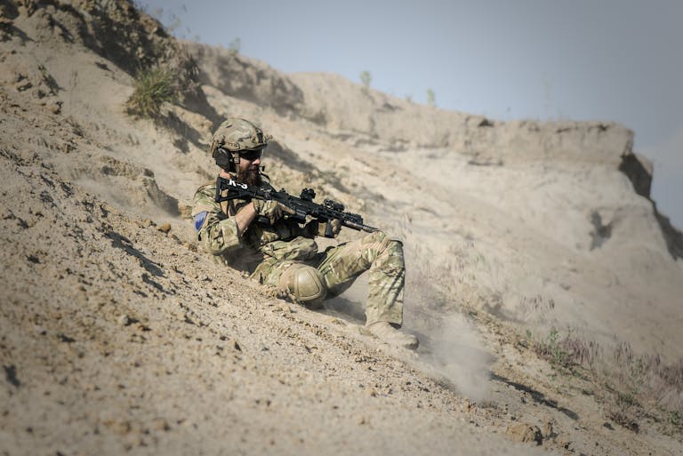 A soldier wearing tactical gear with a rifle in a desert environment, showcasing military preparedness.