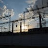 A striking silhouette of an electrical substation with the sun rising behind it, creating a dramatic sky.