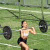 A woman athlete executes a barbell lunge during an outdoor fitness competition.
