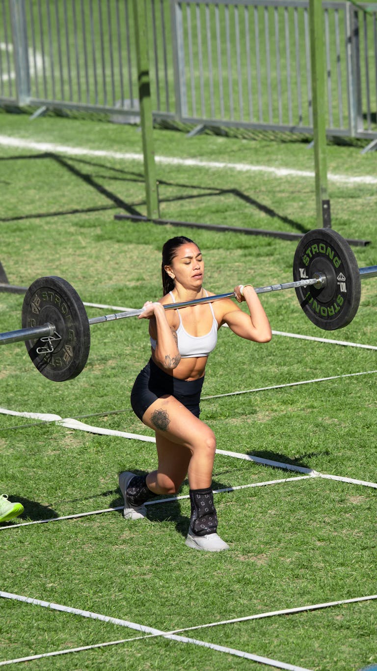 A woman athlete executes a barbell lunge during an outdoor fitness competition.